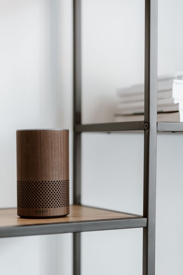 Close-up of a wooden smart speaker on a shelf with books, in a minimalist setting.